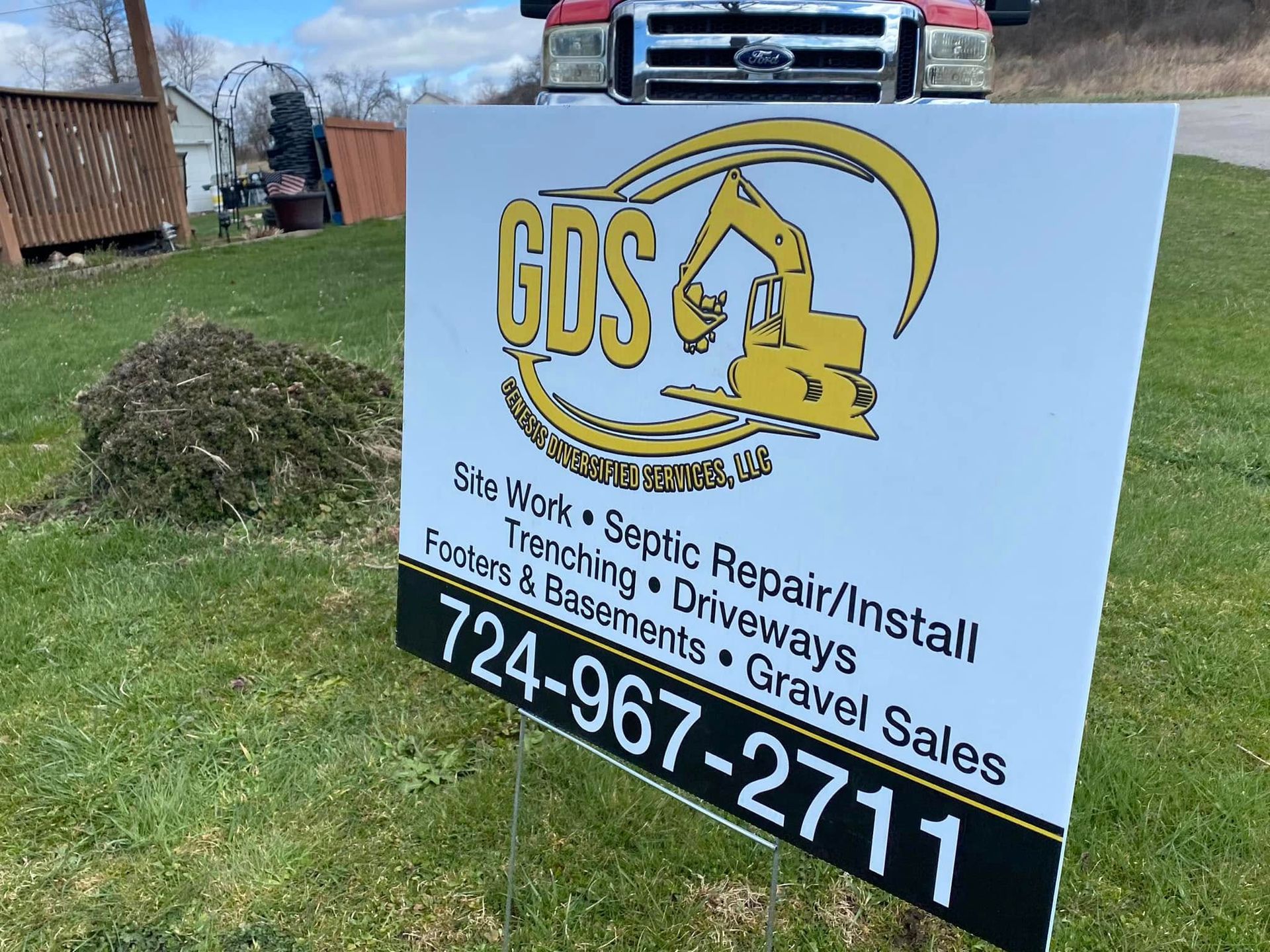 Sign for GDS Excavating on a lawn; a red pickup truck is in the background. The sign lists services and a phone number.
