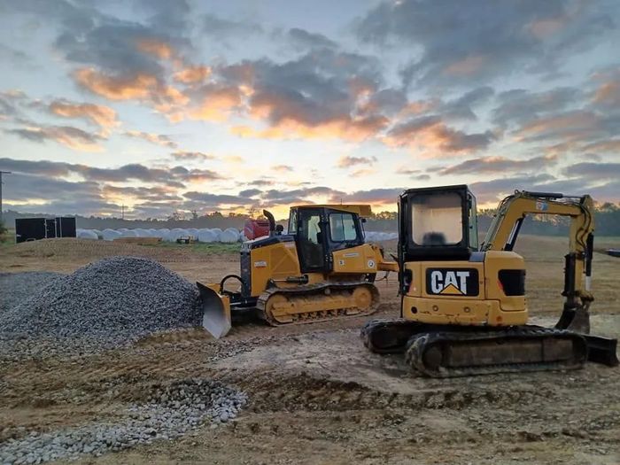 Two yellow Caterpillar construction vehicles on a construction site at dawn, with a pile of gravel.