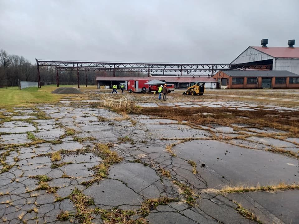 Workers and equipment on a cracked asphalt surface at an industrial site.