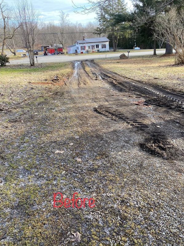 Muddy driveway with tire tracks leading up to a white house in a rural setting. Grass and gravel surround the driveway.
