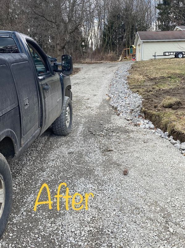 A black truck parked on a newly graveled driveway. The gravel borders a grassy yard and a white garage.