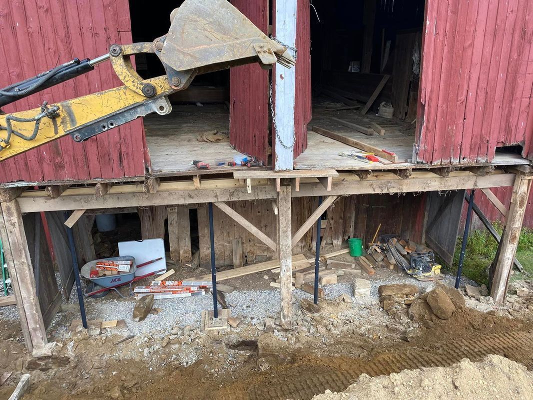 Excavator working on a weathered red barn foundation.