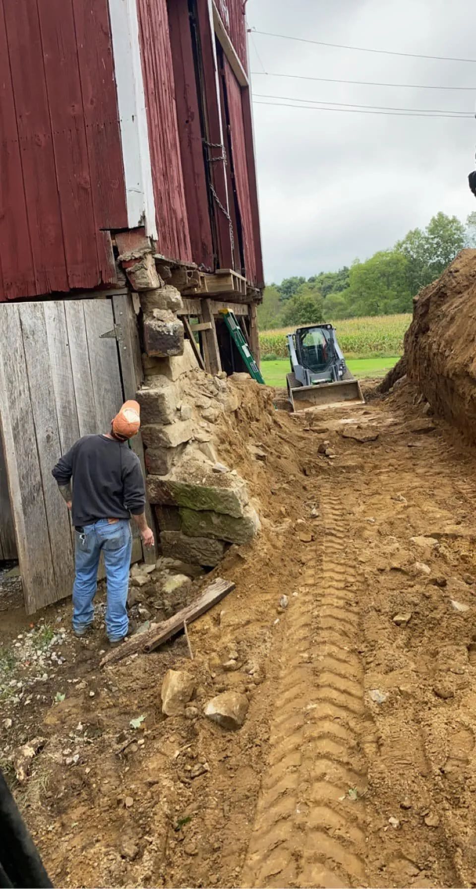Construction workers excavate around the foundation of a red barn.