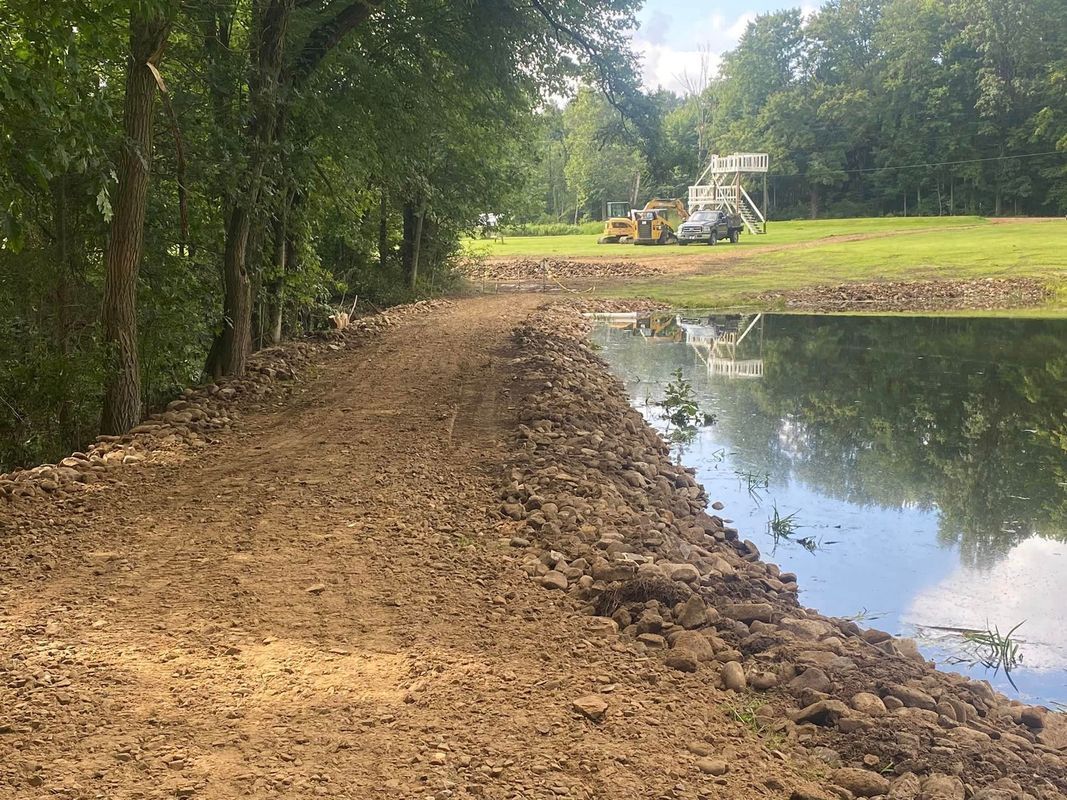 A muddy embankment next to a pond with construction equipment in the background.