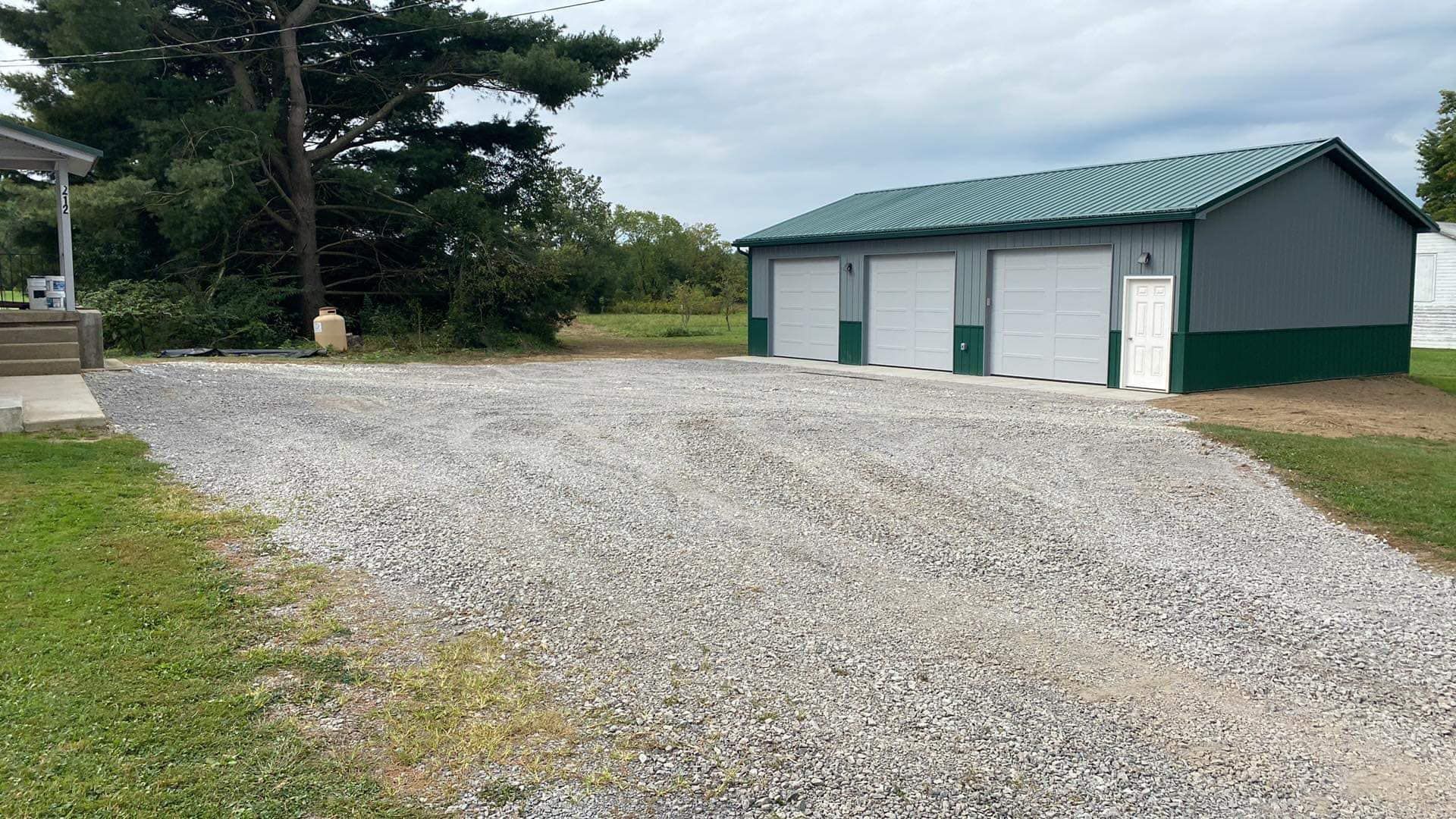 Gravel driveway leading to a three-car garage with a green roof and green trim. Overcast sky.