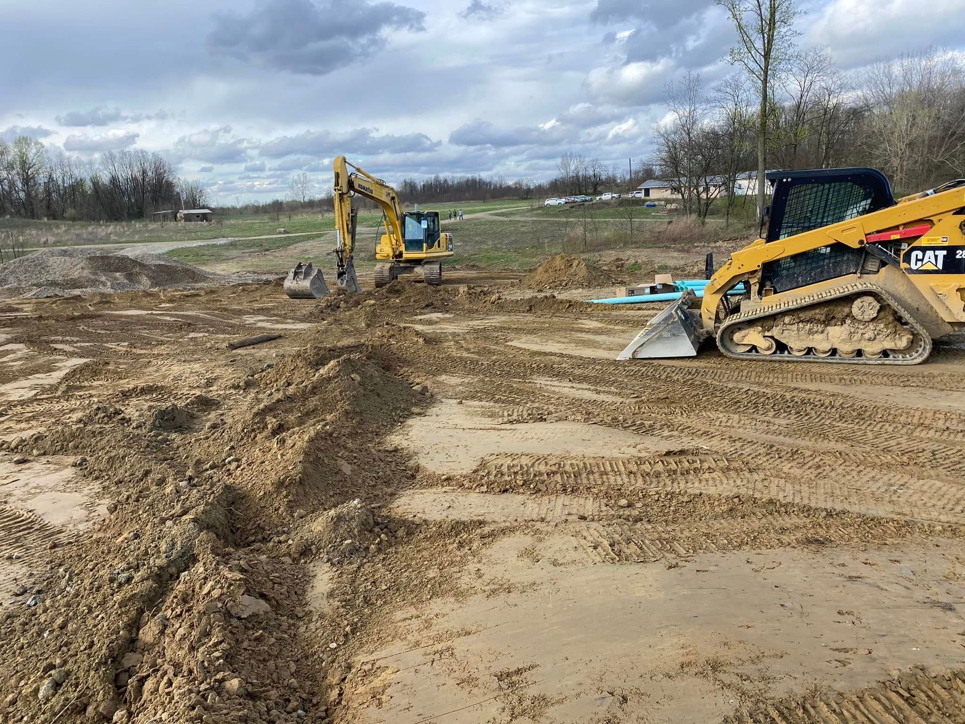 Construction site with yellow excavators digging trenches in brown soil, a cloudy sky overhead.