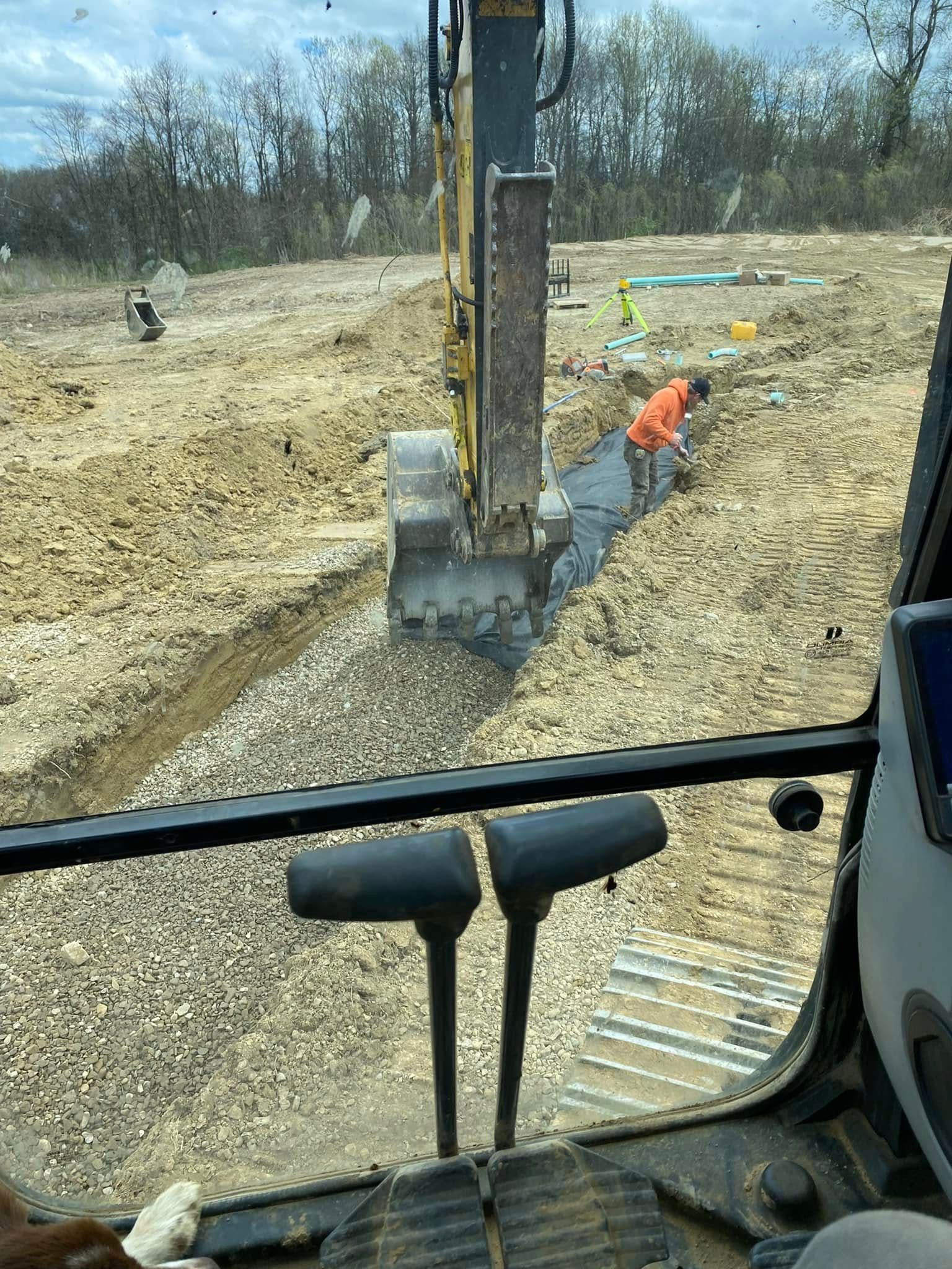 View from excavator cab of worker in orange vest near trench and machinery.