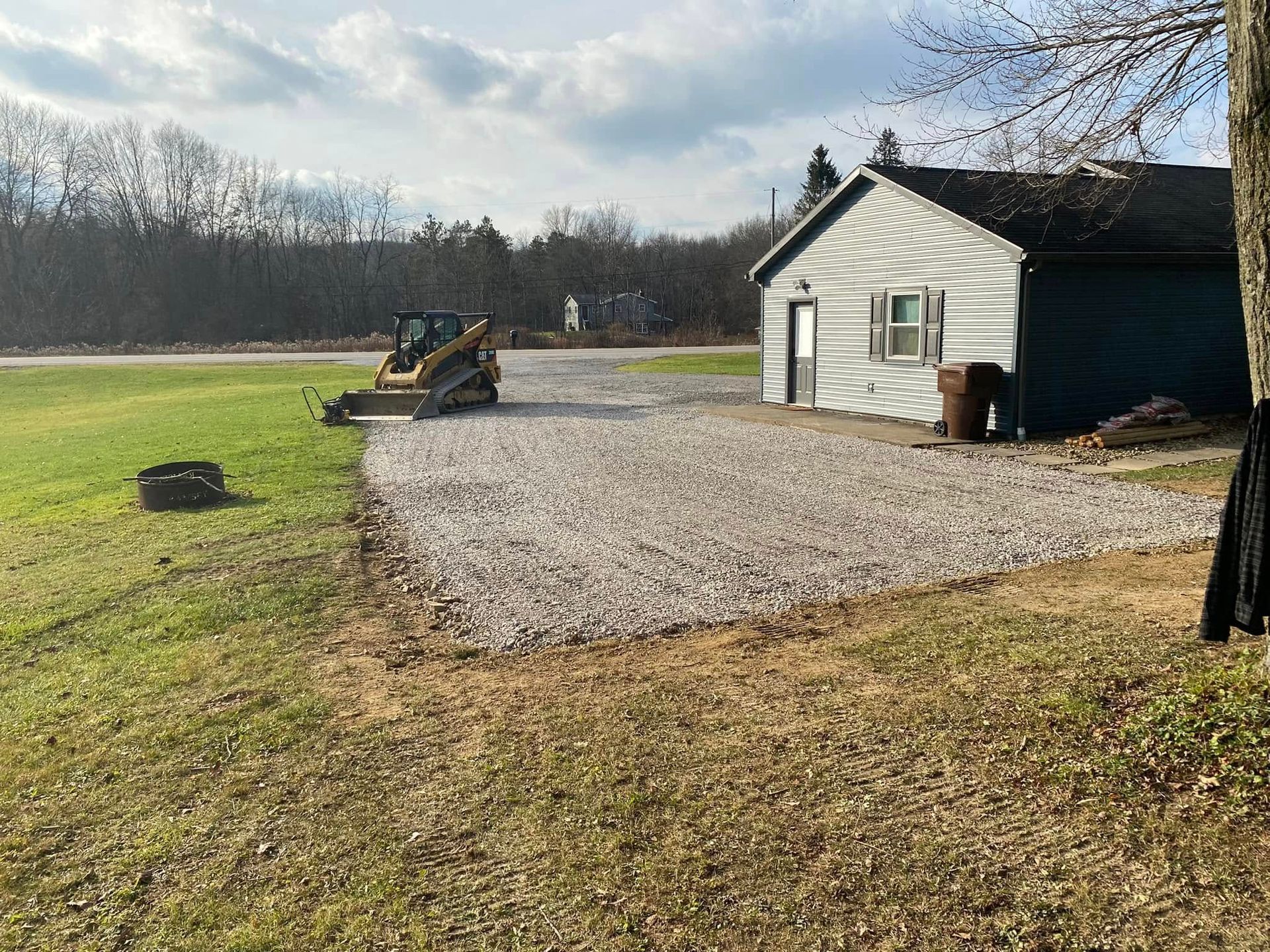 A gravel parking area next to a small, gray building with a yellow construction vehicle parked on it.