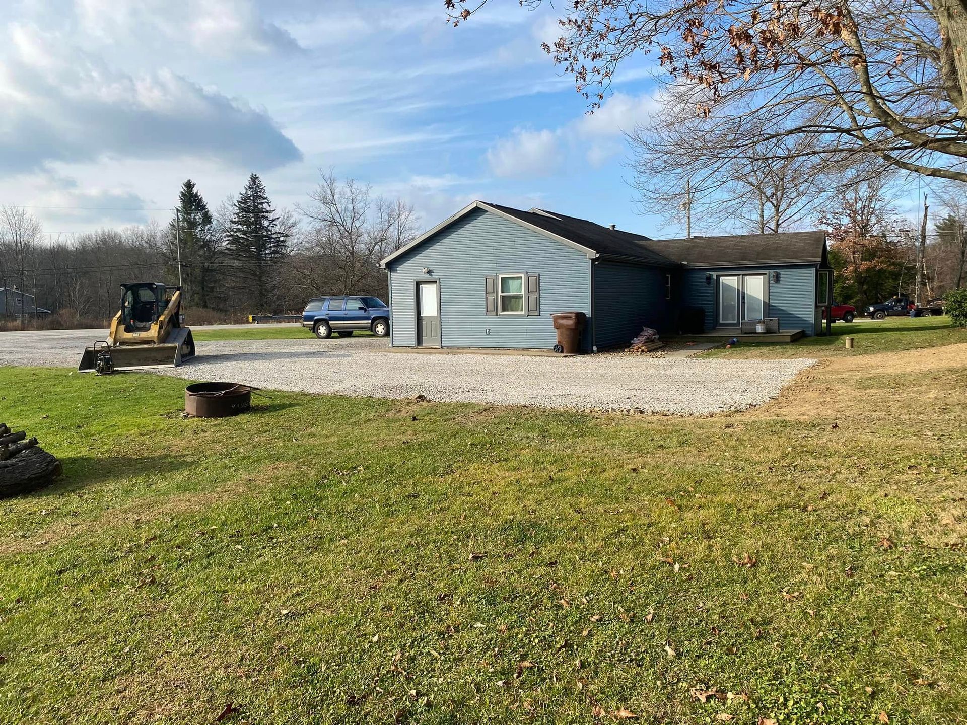 A small blue house with a gravel driveway, a yellow construction vehicle, and green grass.