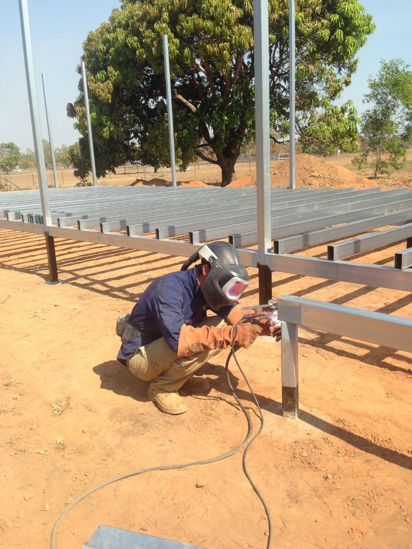 A man is welding a metal structure in the dirt — Local Builders in Yarrawonga, NT