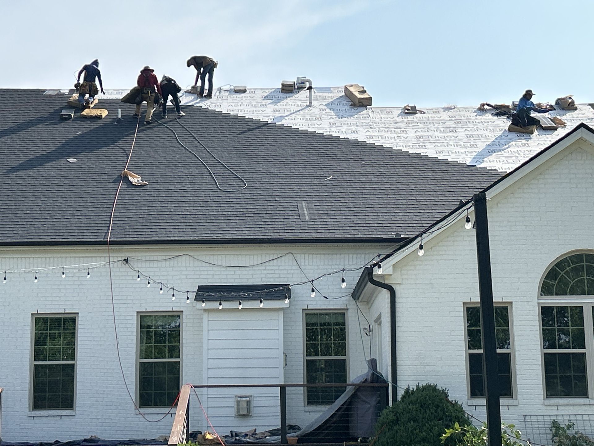 A group of people are working on the roof of a white house.