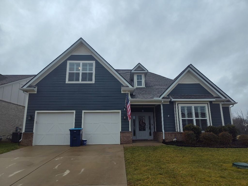 A large house with a blue siding and white garage doors on a cloudy day.