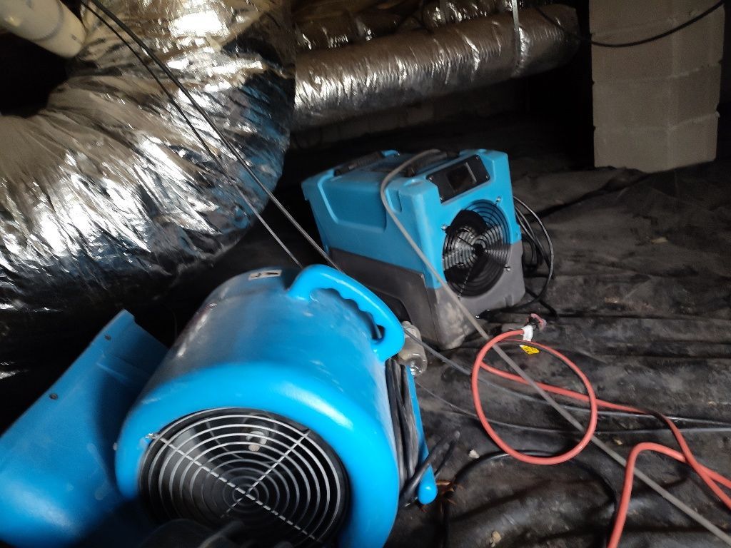 A blue fan is sitting on the floor next to a duct.