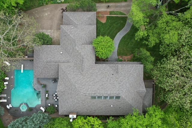 An aerial view of a house with a pool surrounded by trees.