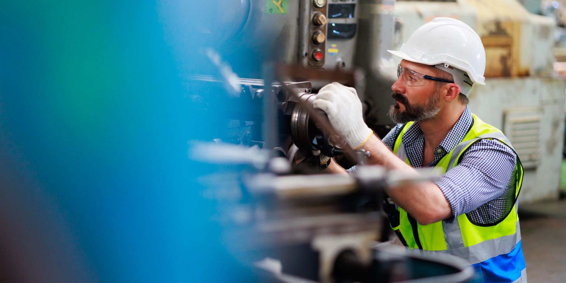 Un homme portant un casque et un gilet de sécurité travaille sur une machine dans une usine.