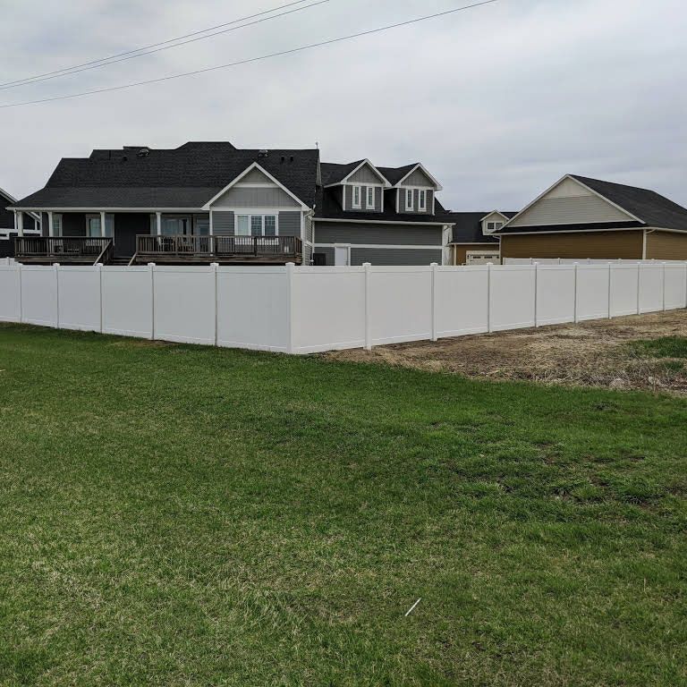 White vinyl fence surrounding two-story house and yard, under overcast sky.