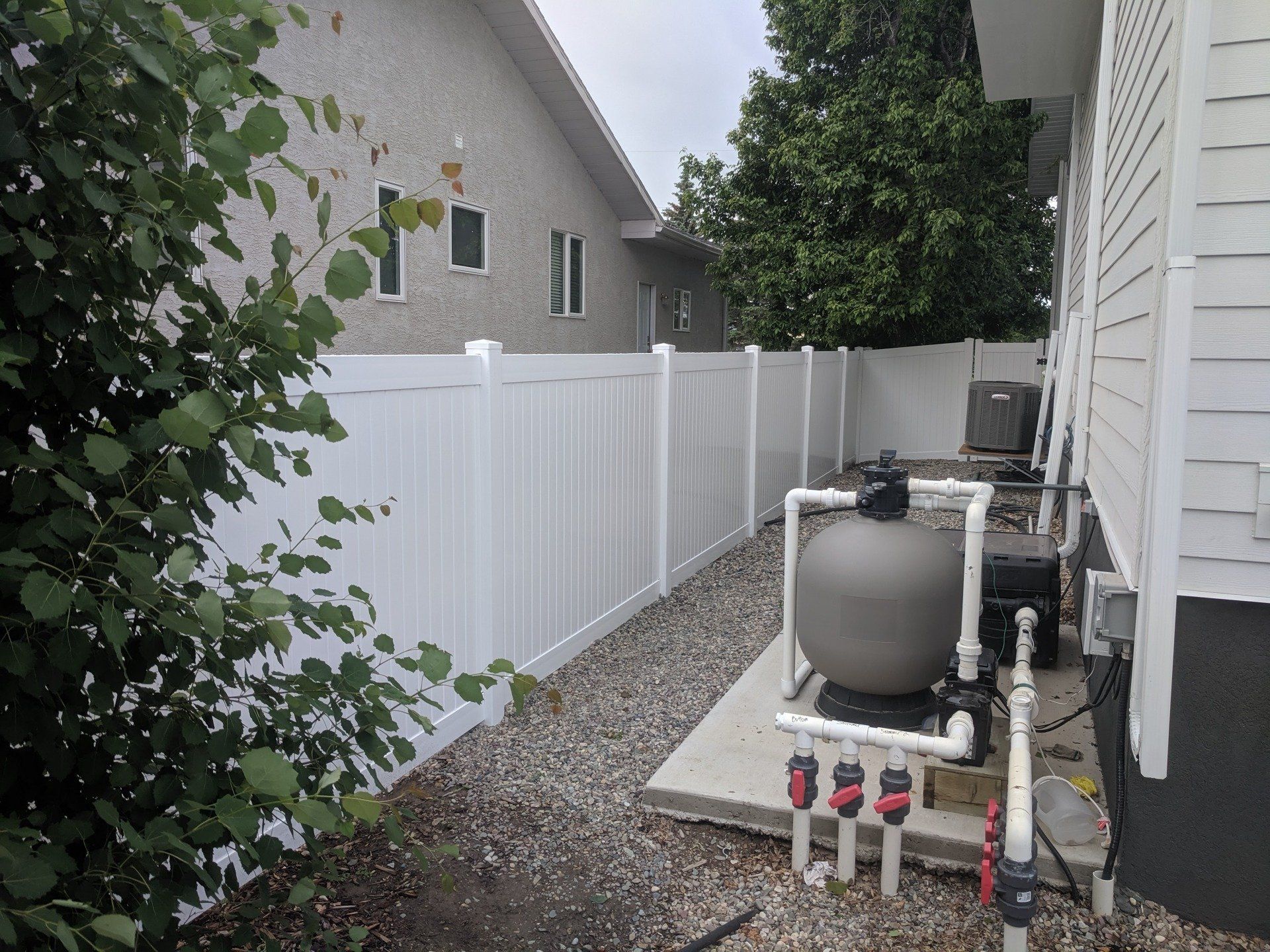 White vinyl fence alongside a building with pool equipment and gravel.