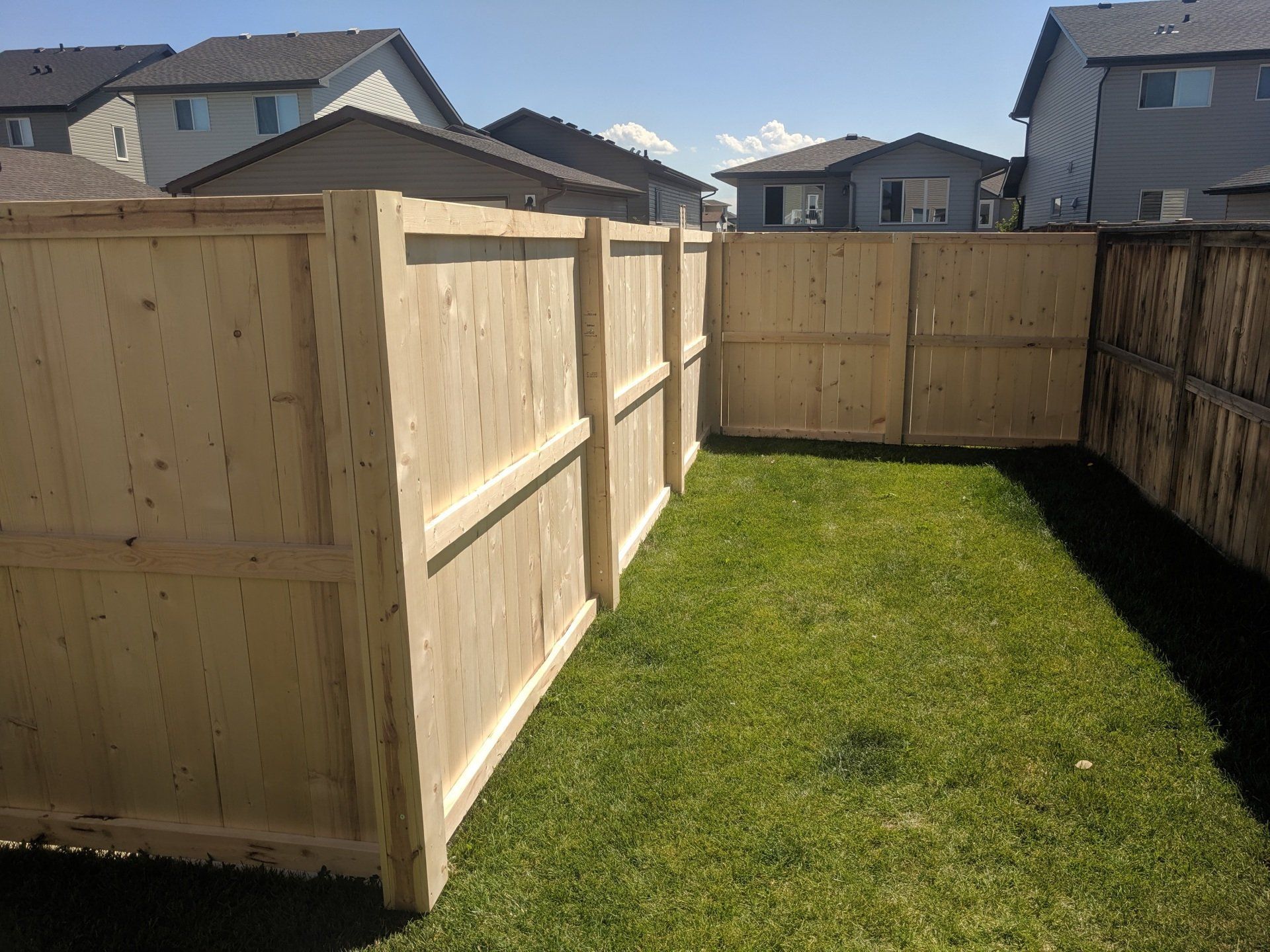 Wooden fence enclosing a small, grassy backyard in a residential area.