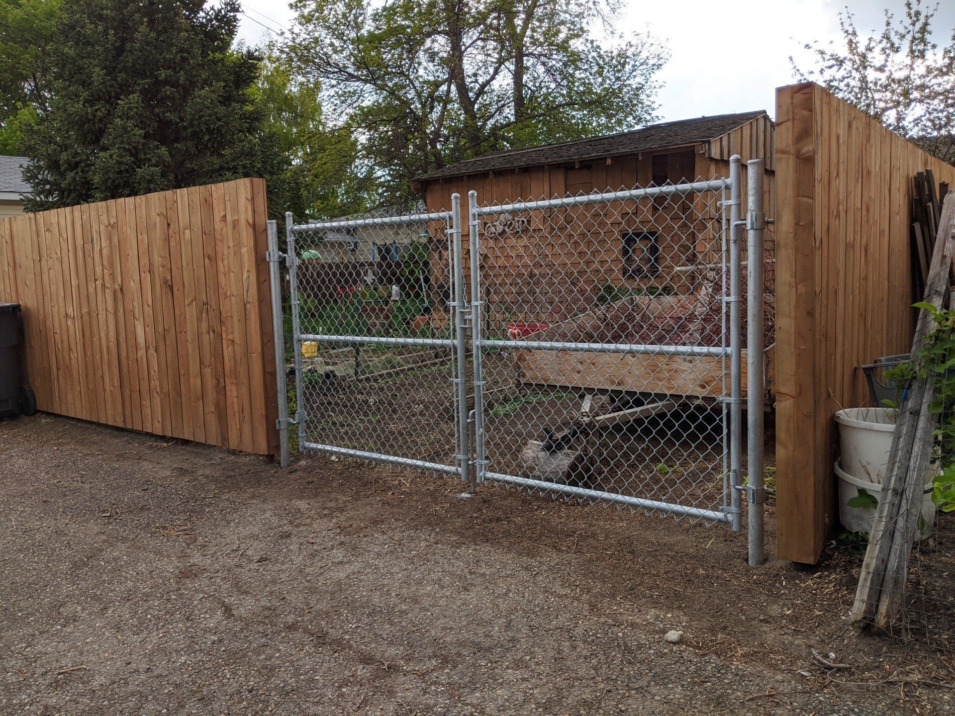 Chain-link double gate in wooden fence, gravel driveway.