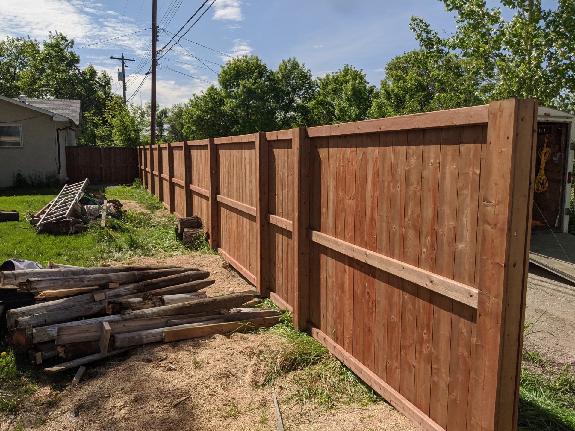A newly built brown wooden fence in a grassy backyard on a sunny day.