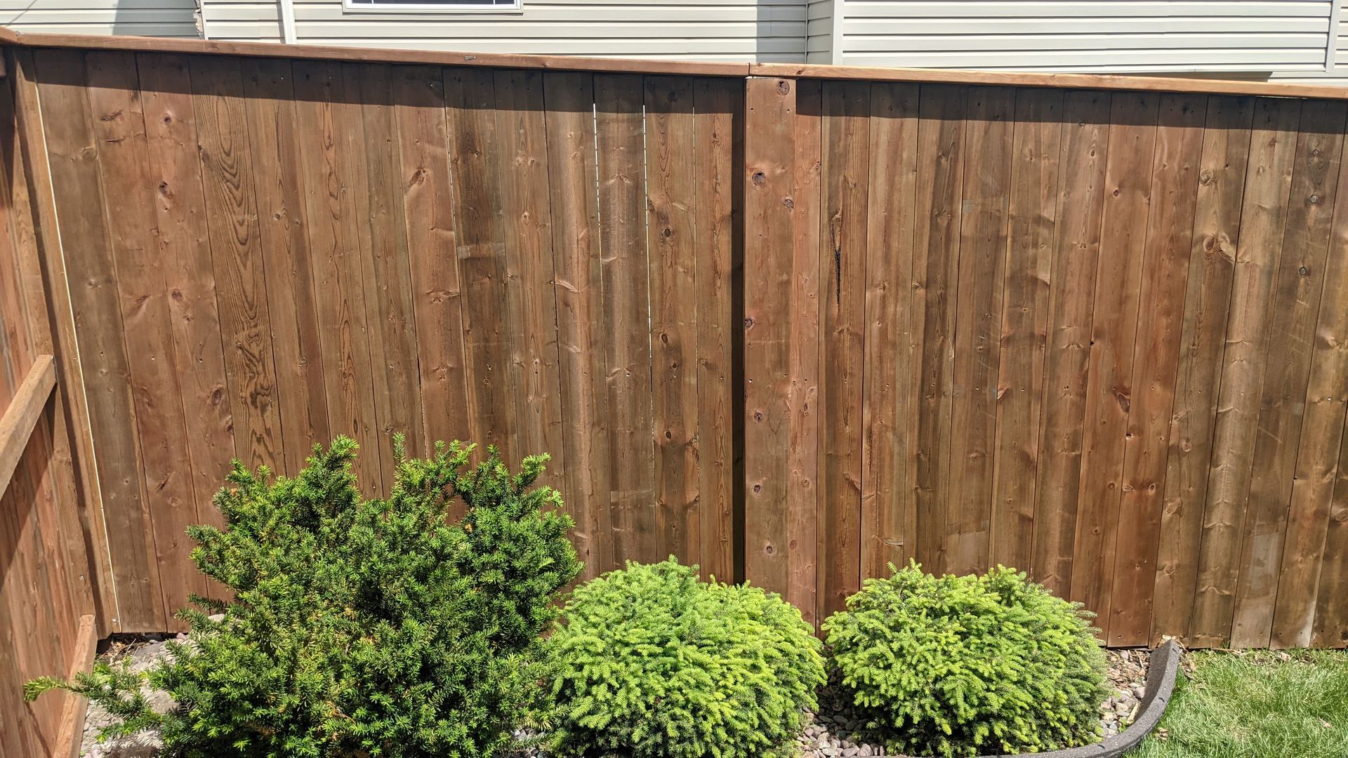 Brown wooden fence with green shrubs planted in front.