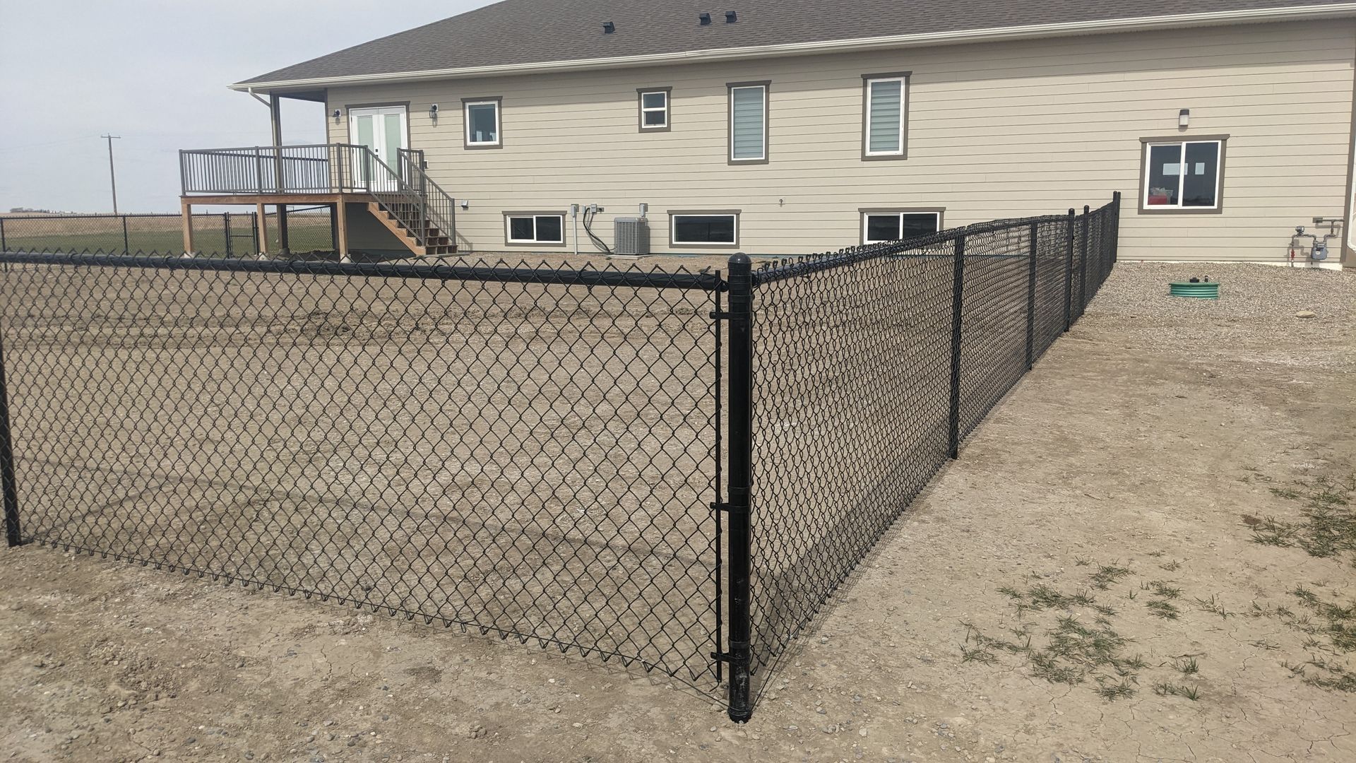 Black chain-link fence enclosing a yard, next to a two-story beige house.