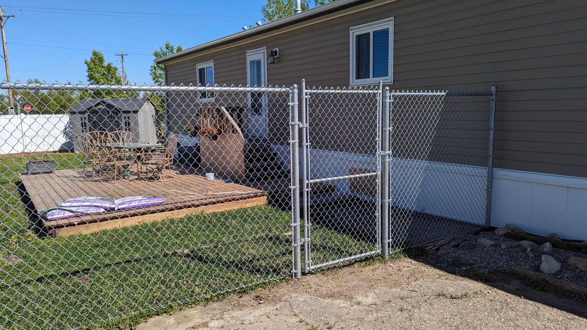 Chain-link fence with gate leading to a backyard with a wooden deck and building.