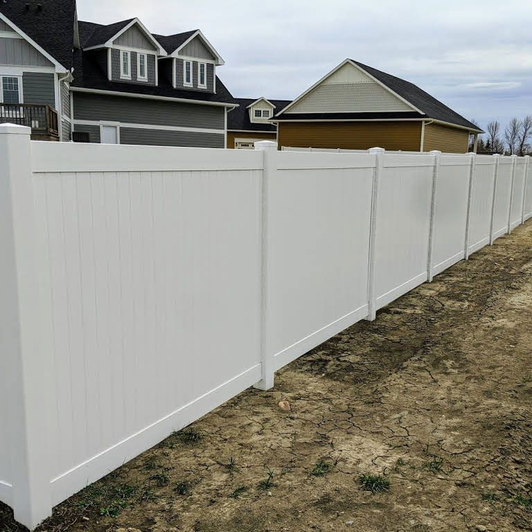 White vinyl fence bordering a grassy area with houses in the background.