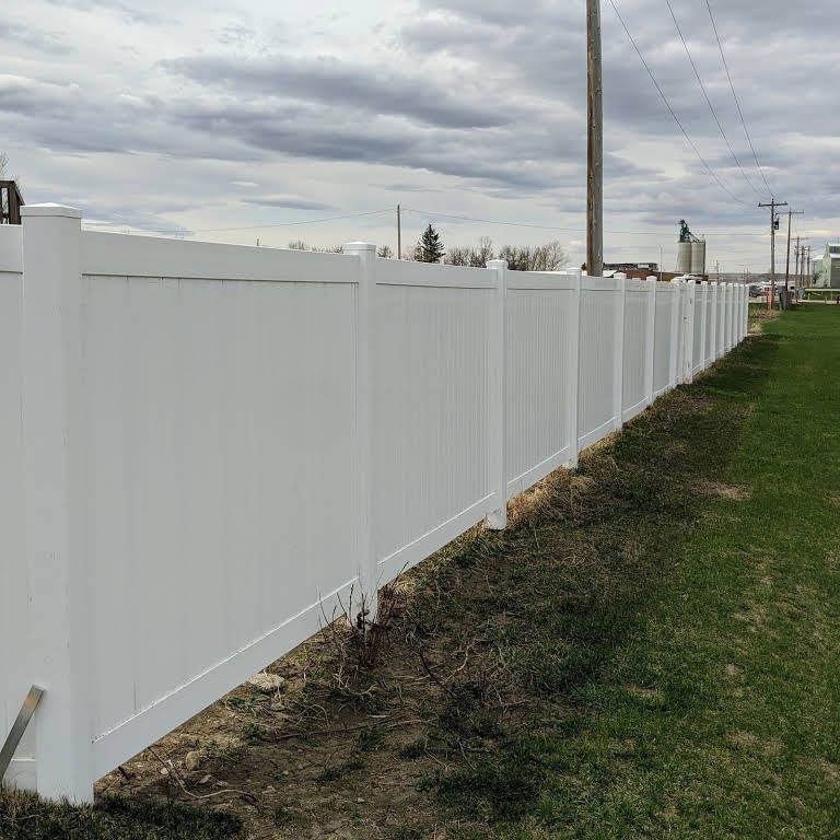 White vinyl fence stretching along a grassy area under a cloudy sky.