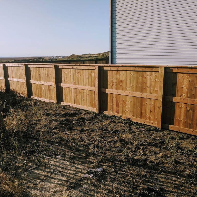 Wooden privacy fence in front of a building, set against a grassy backdrop on a sunny day.