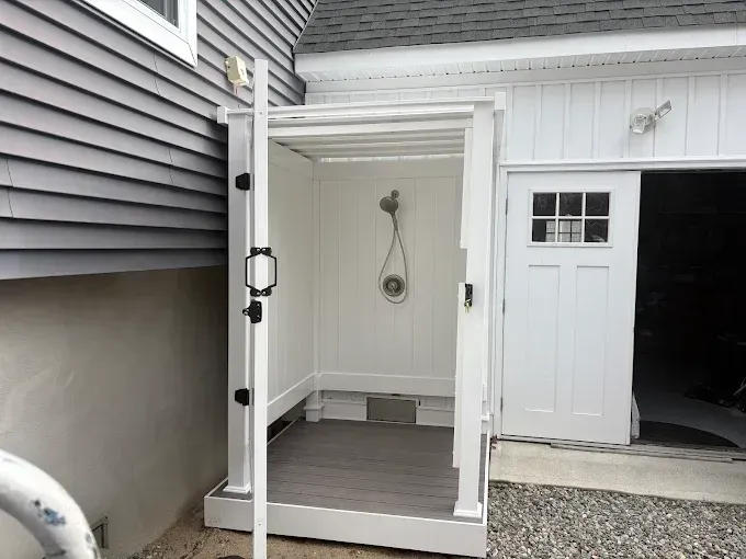 A white outdoor shower is sitting next to a white garage door.