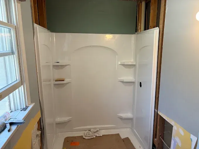A white shower stall is being installed in a bathroom.
