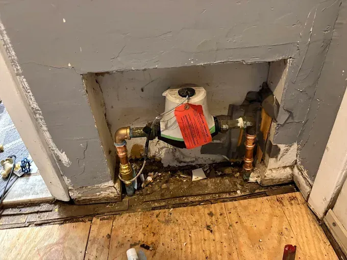 A pipe with a red tag on it is in a hole in the wall.