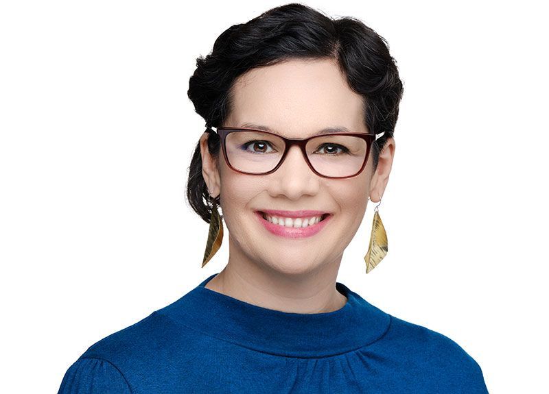 A woman wearing glasses and a black and white polka dot shirt is smiling.