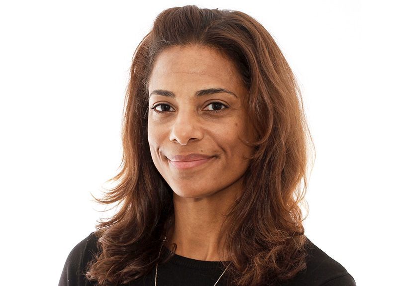 A woman with long brown hair is smiling and wearing a black shirt.
