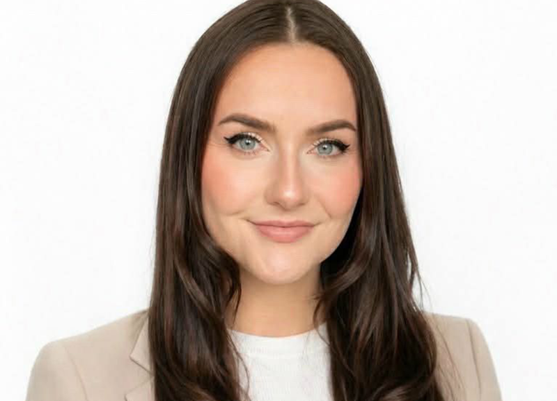 Portrait of a woman with long dark hair, wearing a beige blazer over a white top, against a white background