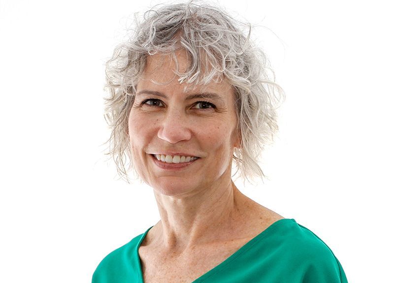 A woman with gray hair is wearing a green shirt and smiling.