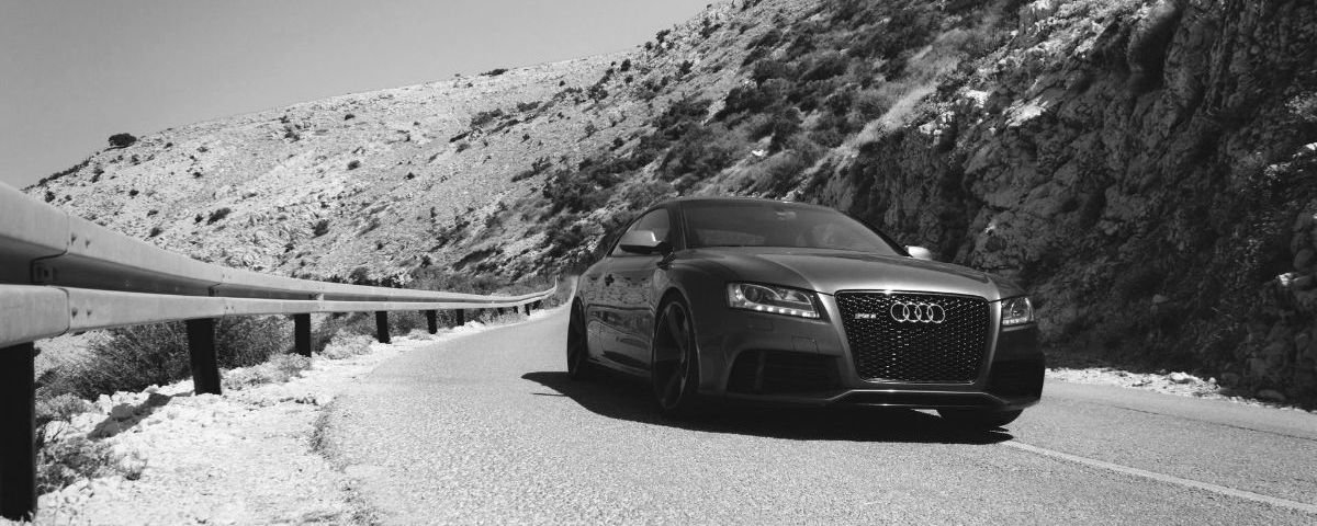 A black and white photo of a car driving down a mountain road.