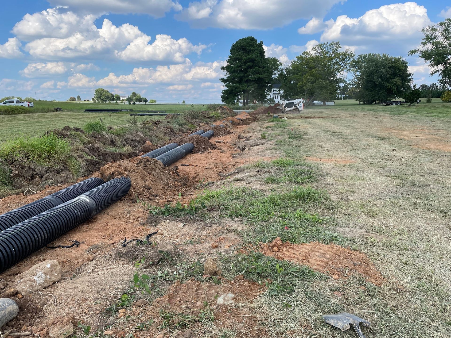 Construction site with corrugated drainage pipes in a trench. A Bobcat in the background. Sunny day.