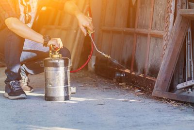 Person spraying insecticide near a wooden structure.