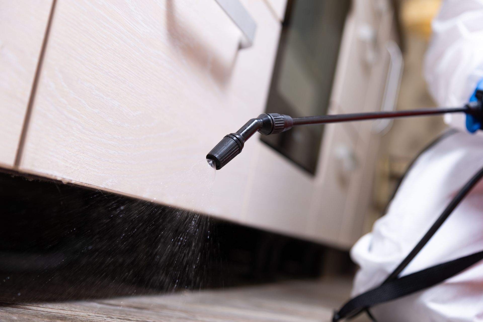 Person in protective suit sprays insecticide near cabinet. Person in protective suit sprays insecticide near cabinet.