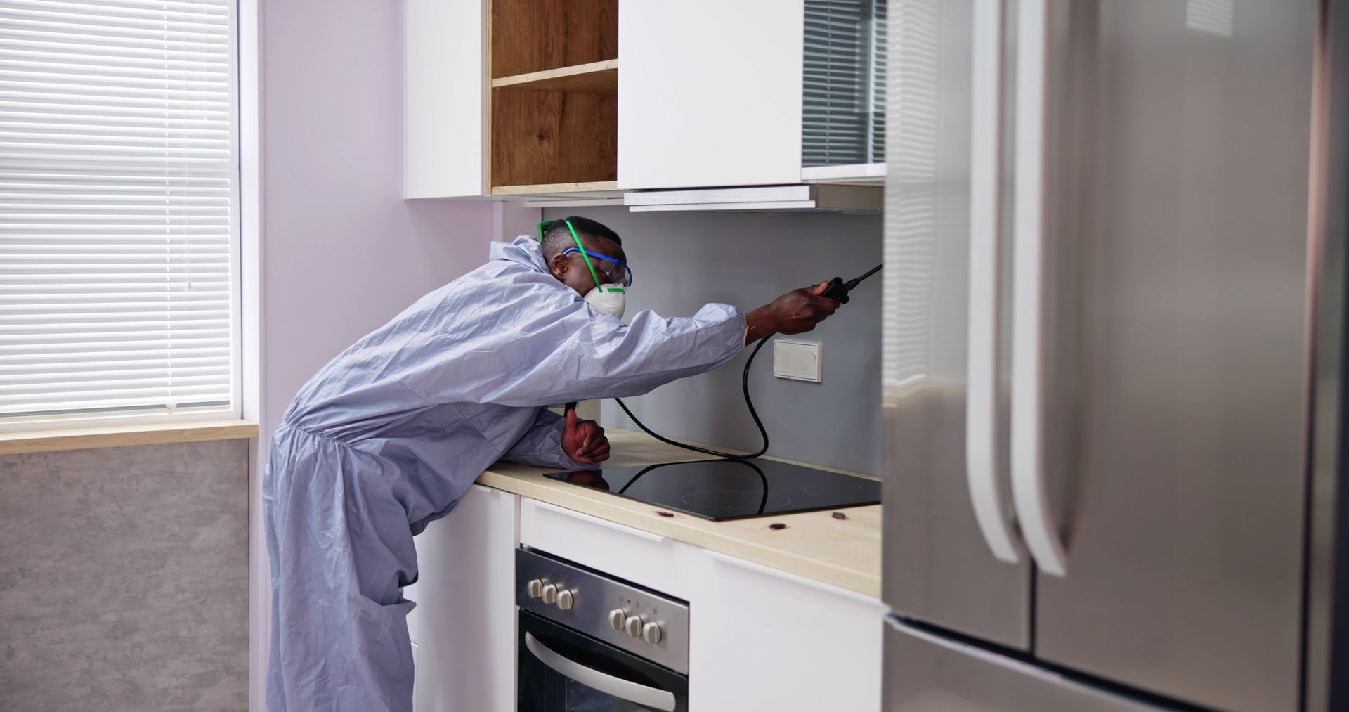 Pest control worker spraying insecticide in a kitchen, wearing protective gear. Pest control worker spraying insecticide in a kitchen, wearing protective gear.