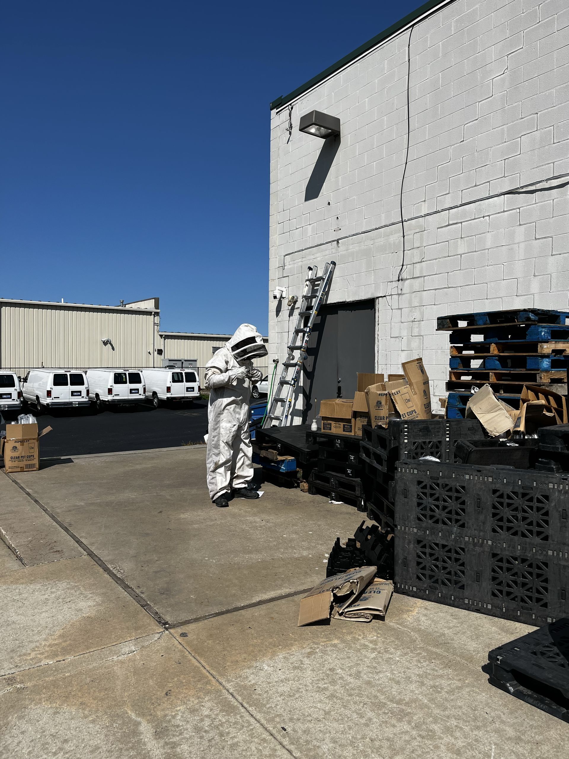 Pest control worker spraying insecticide along a cabinet baseboard. Yellow tank in the background.