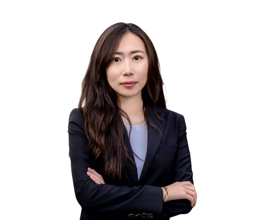 A woman in a suit is standing with her arms crossed and smiling.