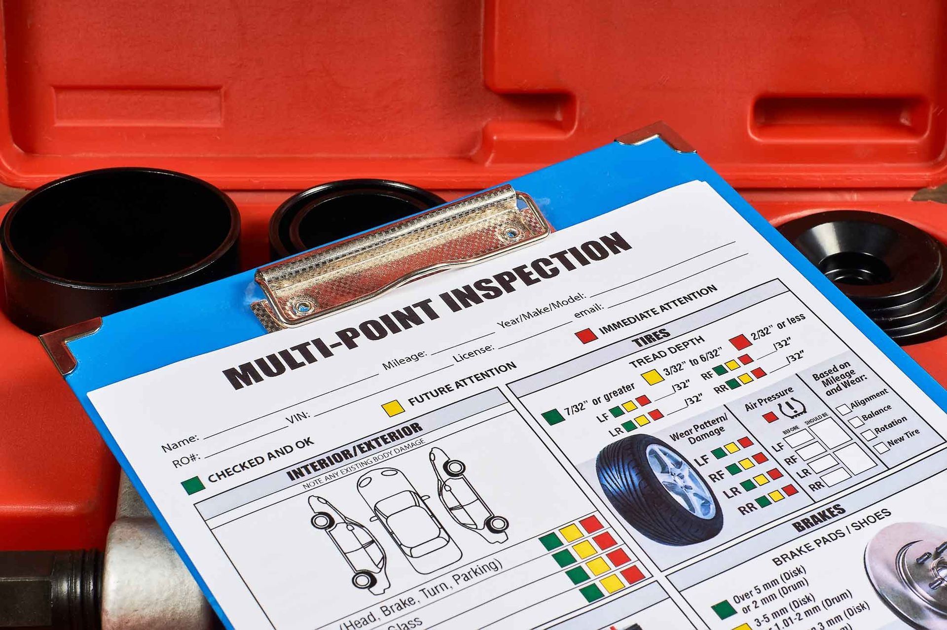 A multi-point inspection checklist on a blue clipboard, next to tools in a red toolbox. The checklist shows car diagrams and colored indicators. A multi-point inspection checklist on a blue clipboard, next to tools in a red toolbox. The checklist shows car diagrams and colored indicators.