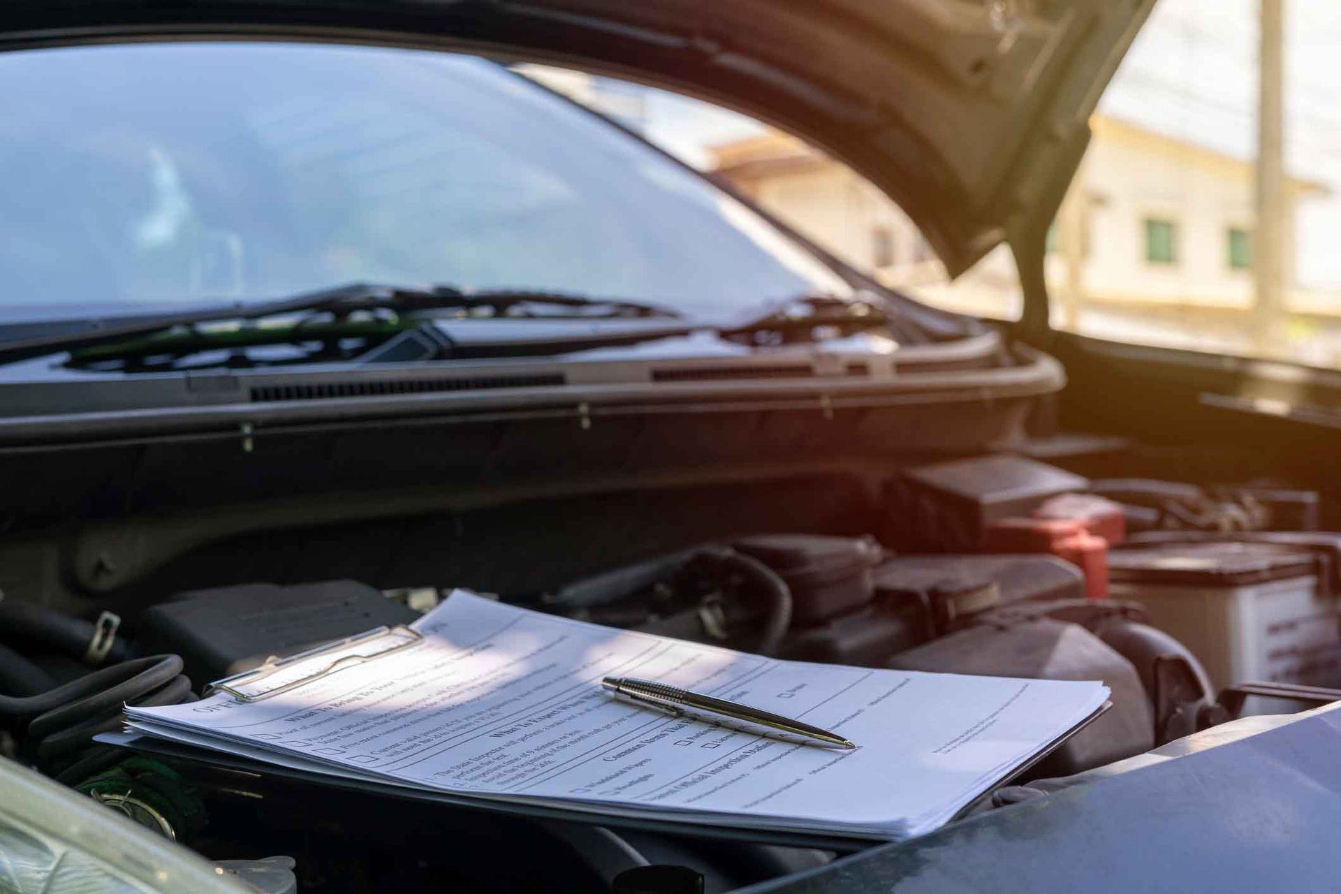 Car engine bay with open hood. A document and pen rest on the engine, suggesting car maintenance or repair. Car engine bay with open hood. A document and pen rest on the engine, suggesting car maintenance or repair.