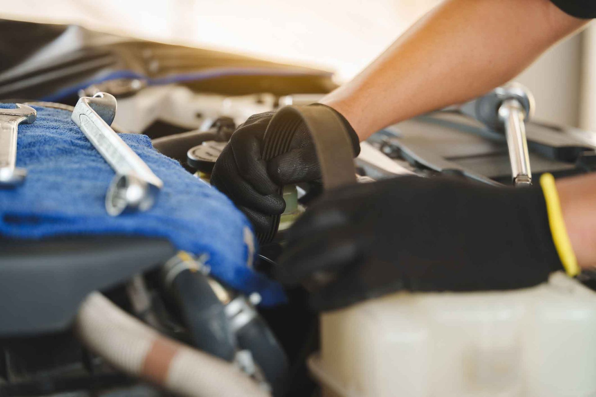 Mechanic working on a car engine; wearing black gloves, using tools in a garage setting. Mechanic working on a car engine; wearing black gloves, using tools in a garage setting.