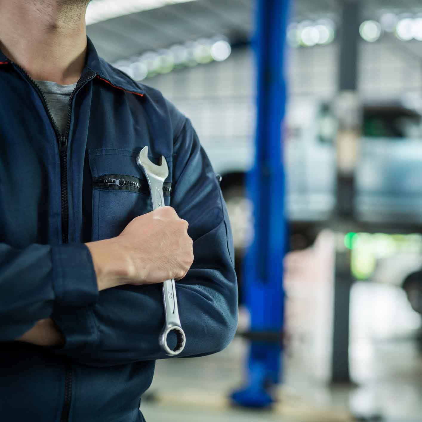 Mechanic in a blue jumpsuit holding a wrench, standing in a car repair shop.