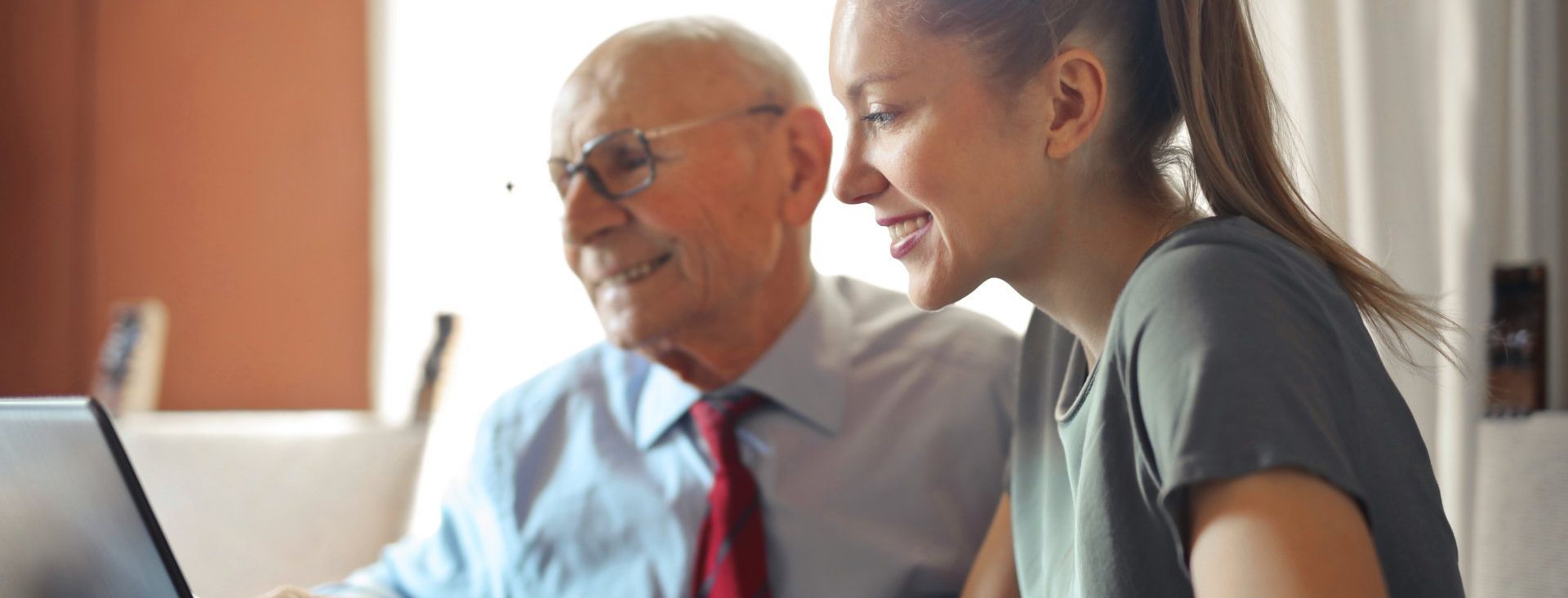 An elderly man and a young woman are looking at a laptop computer.