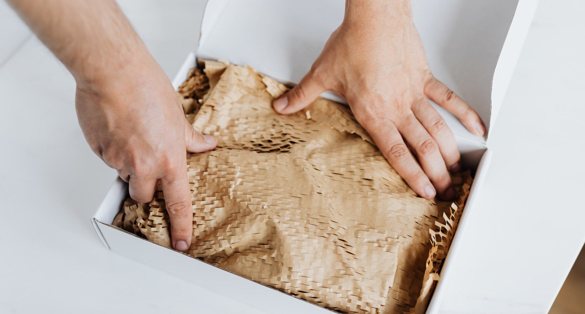 A person is packing a box with brown paper.